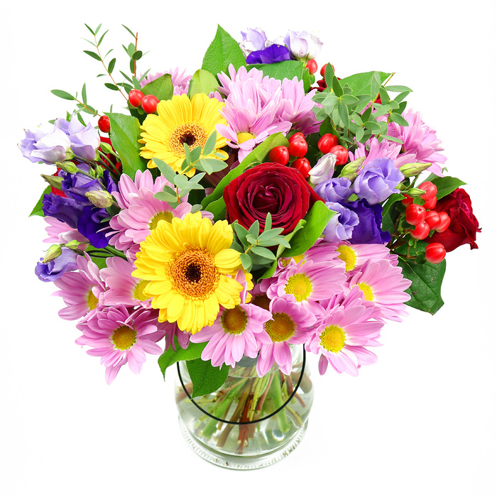 A tall, rounded bouquet of mixed seasonal flowers fills a clear glass vase, the entire design set against a plain white background so the rich colours and textures truly shine. At the centre, deep red roses cluster closely together, their velvety petals unfolding in textbook spirals that suggest affection, admiration, and a timeless romantic touch. Just in front of them, two bright yellow gerbera daisies with dark brown-orange centres tilt forward, their bold discs echoing sunshine and instantly lifting the mood, much like a bright morning over the rooftops of Sipson. Surrounding these focal blooms, an abundance of soft pink and pale lilac daisies or chrysanthemums fans outward, each head packed with petite, fine petals and tiny golden centres, creating a halo of pastel softness that gives the bouquet generous volume. Threaded through this cushion of daisies are elegant purple and lavender lisianthus flowers, their slender, bell-like blooms and gently crimped edges adding a note of cool elegance and depth, reminiscent of shadows stretching across nearby village greens. Punctuating the flowers are clusters of smooth, round red hypericum berries, their glossy skins catching the light and bringing a playful, contemporary feel. Different shades of green foliage, from dark, substantial leaves to light, airy sprigs, weave in and out, framing the blossoms and adding a natural, freshly gathered look. Through the clear vase, the straight stems can be seen arranged neatly in clean water, evidence of experienced hands at work, such as those at Flowers Sipson preparing arrangements for local homes and businesses. The composition feels joyful, balanced, and inviting - a bouquet that could celebrate a birthday, welcome a new neighbour, or simply bring a touch of floral warmth into a Sipson living room.